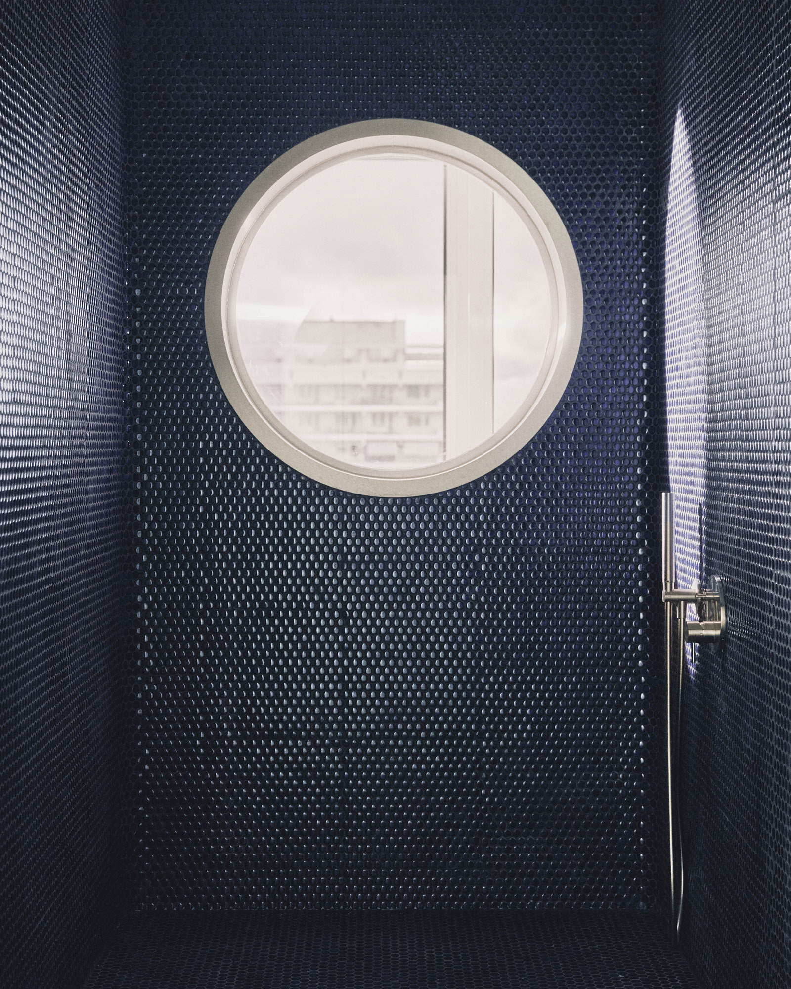 L48 bathroom — dark navy mosaic tiles and round porthole window